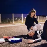 Una mujer llama a emergencias junto a un hombre tendido en la carretera. A su lado, un botiquín abierto. ¿Qué significa pas? ¿Una vida en peligro?