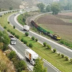 Autopista con camiones y tren de carga. Un viaje escénico de Burgos a Zaragoza sin peaje, con paisajes verdes y campos.