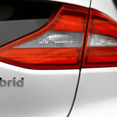 Detalle de la parte trasera de un coche blanco con la palabra "hybrid" en relieve. Las luces traseras rojas y blancas son visibles.