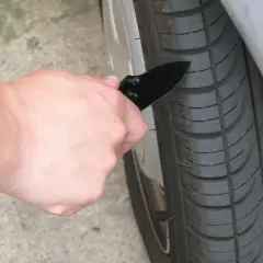 Mano con navaja revisando la banda de rodadura de un neumático, para saber si tengo una rueda pinchada.