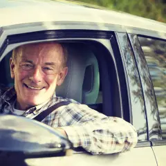 Hombre mayor sonriente al volante. Las personas mayores suelen tener menos accidentes en situaciones de conducción tranquila y familiar.