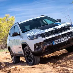 El Jeep Compass Trailhawk 4xe blanco se aventura por un camino de tierra, demostrando su capacidad todoterreno bajo un cielo azul.