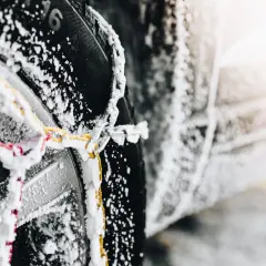 Primer plano de cadenas de nieve cubiertas de escarcha sobre un neumático de coche, mostrando cómo colocar cadenas de nieve para la seguridad invernal.