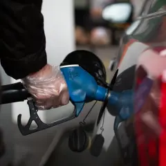 Persona con guantes pone boquilla de surtidor en coche. Un dispositivo para disminuir consumo de gasolina.