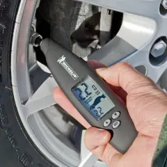Mano revisa la presión neumaticos con un medidor digital Michelin. Muestra 2.2 bares de presión actual y objetivo.