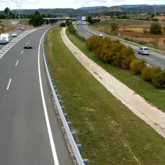 Autopista con varios coches y caravanas. Se aprecian las áreas de servicio AP2 al fondo, con vegetación y campos.