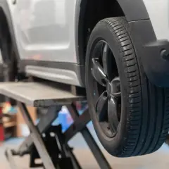 Un coche en un elevador, listo para cambiar 2 ruedas o las 4. Se ve el neumático y la llanta negra.