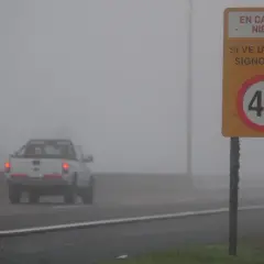 Camioneta blanca avanza en **niebla densa** bajo un **alumbrado** de señalización vial que indica 40 km/h.