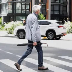 Hombre mayor cruza la calle con paraguas. Las personas mayores pueden tener problemas como peatones, especialmente con el tráfico moderno.