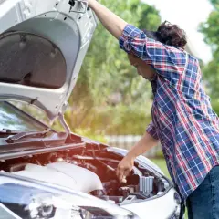 Persona revisa el motor de su coche tras un **siniestro vial**. El capó está abierto y ella busca la causa del problema.