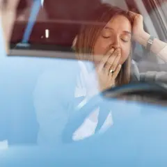 Mujer bostezando en el coche. Para disminuir la probabilidad de somnolencia debe evitar conducir.