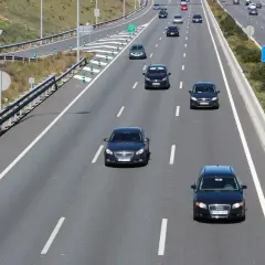En el carril de entrada, ¿cómo debe circular? Un coche negro circula por el carril de entrada de una autopista, con otros vehículos delante y detrás.