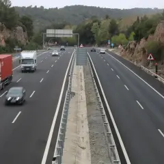 Tráfico en las autopistes catalanes, con camiones y coches circulando por una carretera de varios carriles rodeada de vegetación y rocas.