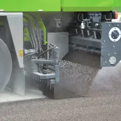 Máquina esparciendo material granular sobre el asfalto, parte de un proceso de reciclado.