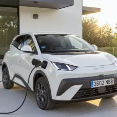 Coche híbrido blanco cargando en la entrada de una casa moderna. Averigua cuanto cuesta cargar un coche hibrido.