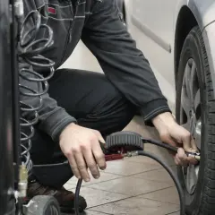 Hombre agachado conectando una manguera a la válvula de un neumático para reparar pinchazo coche.