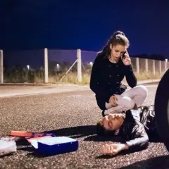 Una mujer llama a emergencias junto a un hombre tendido en la carretera. A su lado, un botiquín abierto. ¿Qué significa pas? ¿Una vida en peligro?