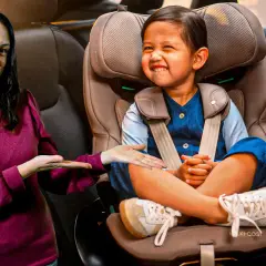 Una mujer sonríe mientras señala a un niño feliz sentado en su silla de coche. ¡Los niños en el coche están seguros y contentos!