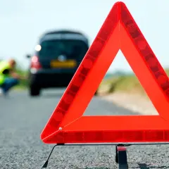 Triángulo de señalización de emergencia en carretera. Un coche averiado y una persona con chaleco reflectante en el fondo. Esquema pas.