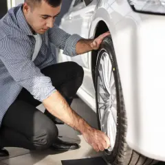 Hombre revisando la rueda de un coche blanco, asegurándose de que el neumático tenga el código velocidad correcto para un viaje seguro.