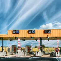 Estación de ap2 peajes bajo un cielo azul con nubes. Carriles de pago con barreras y señales de tráfico.