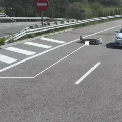 Un coche blanco se detiene cerca de un parachoques dañado en la carretera, indicando un accidente por objeto en la carretera.