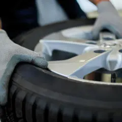 Manos enguantadas sostienen un neumático y llanta, listos para su reparación.