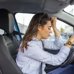 Mujer con la mano en la frente, sufriendo ansiedad al conducir.