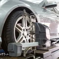 Un coche plateado en un taller mecánico recibe servicio de alineación de ruedas con equipo especializado.