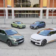 Cuatro coches Kia, dos hibridos y electricos, en tonos verde, azul y blanco, frente a un edificio moderno.
