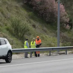 Personal de autopistas atiende un incidente en la carretera. Un coche blanco y una furgoneta naranja con señalización de emergencia están detenidos.