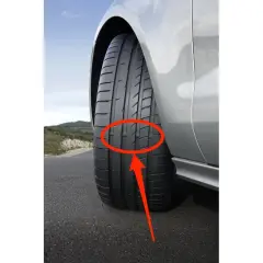 Flecha roja señala los neumáticos desgastados de un coche plateado en una carretera.