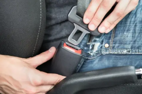 Persona abrochando el cinturón de seguridad en un coche. En un turismo es obligatorio utilizar los cinturones de seguridad.