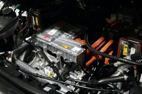 Detalles del motor de un coche eléctrico, listo para su revisión. Cables naranjas de alta tensión y componentes metálicos.