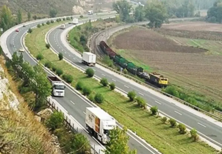 Autopista con camiones y tren de carga. Un viaje escénico de Burgos a Zaragoza sin peaje, con paisajes verdes y campos.