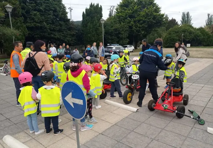 Niños con chalecos reflectantes participan en juegos de educación vial, aprendiendo normas de tráfico con bicicletas y coches de pedales.