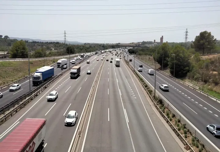 Tráfico intenso en la ap7 Girona, con camiones y coches circulando por la autopista bajo un cielo despejado.