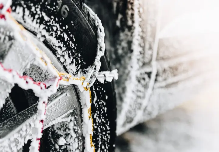 Primer plano de cadenas de nieve cubiertas de escarcha sobre un neumático de coche, mostrando cómo colocar cadenas de nieve para la seguridad invernal.