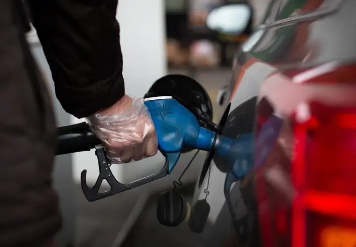 Persona con guantes pone boquilla de surtidor en coche. Un dispositivo para disminuir consumo de gasolina.