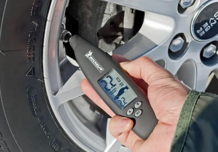 Mano revisa la presión neumaticos con un medidor digital Michelin. Muestra 2.2 bares de presión actual y objetivo.