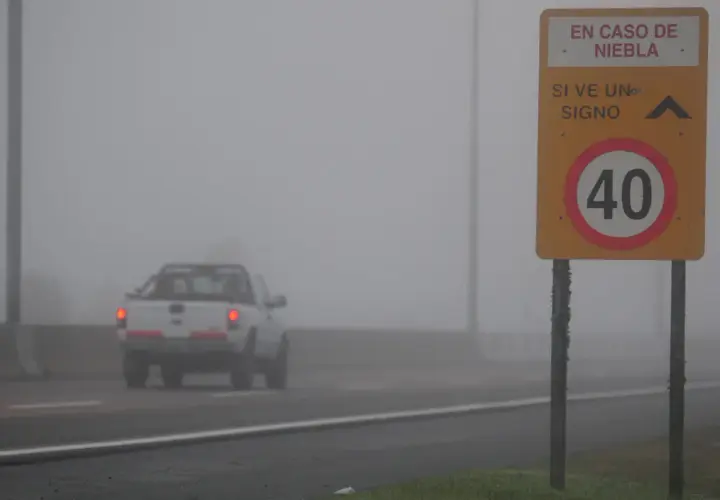 Camioneta blanca avanza en **niebla densa** bajo un **alumbrado** de señalización vial que indica 40 km/h.