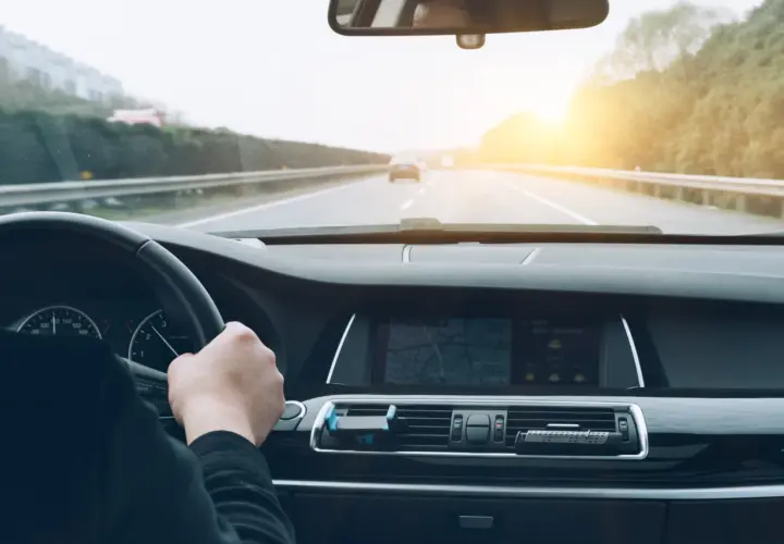 Conduciendo por la autopista, el sol brilla al atardecer. El navegador muestra la ruta, anticipando el pago del vía t peaje.