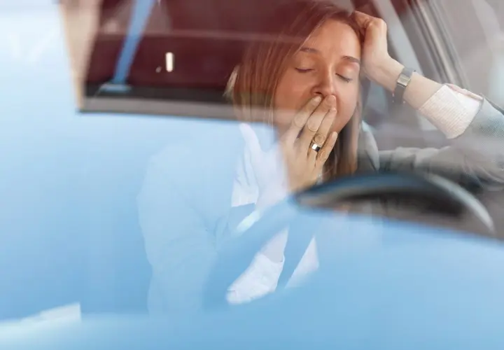 Mujer bostezando en el coche. Para disminuir la probabilidad de somnolencia debe evitar conducir.