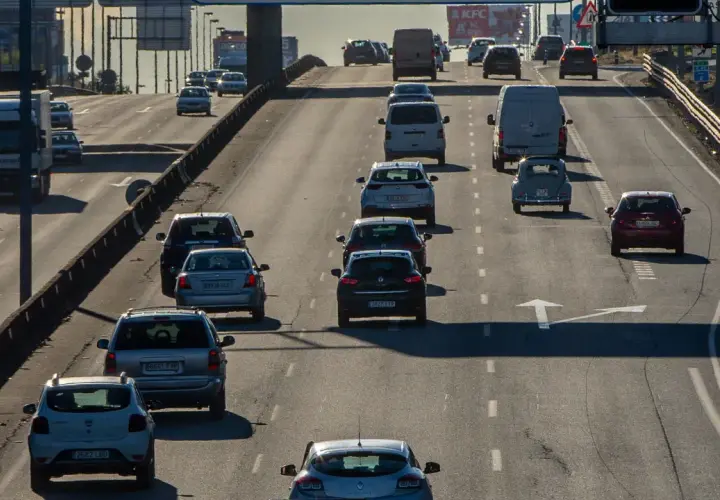 Tráfico denso en autopista, con coches y furgonetas circulando. Se observa señal de tráfico con **mínimo de velocidad en autopista** de 60 km/h.
