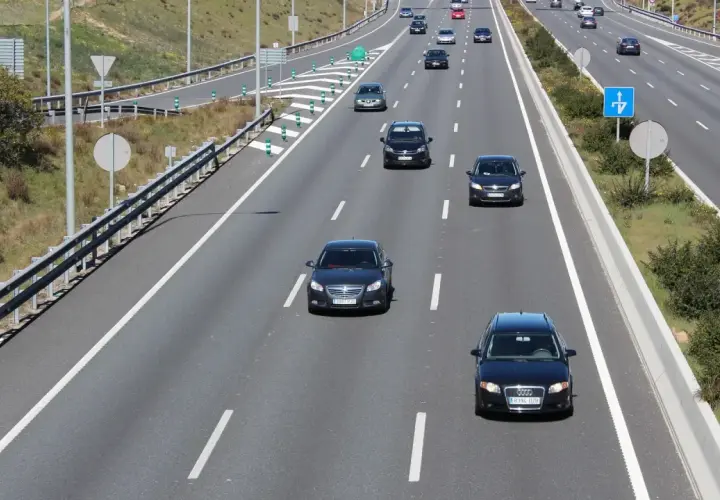 En el carril de entrada, ¿cómo debe circular? Un coche negro circula por el carril de entrada de una autopista, con otros vehículos delante y detrás.