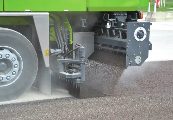 Máquina esparciendo material granular sobre el asfalto, parte de un proceso de reciclado.