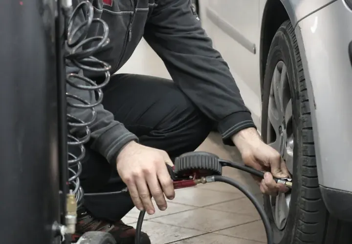 Hombre agachado conectando una manguera a la válvula de un neumático para reparar pinchazo coche.