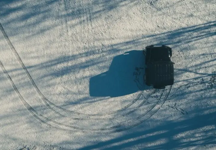 Un vehículo negro deja huellas en la nieve, mostrando cómo conducir con hielo.