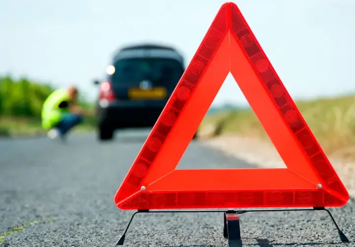 Triángulo de señalización de emergencia en carretera. Un coche averiado y una persona con chaleco reflectante en el fondo. Esquema pas.