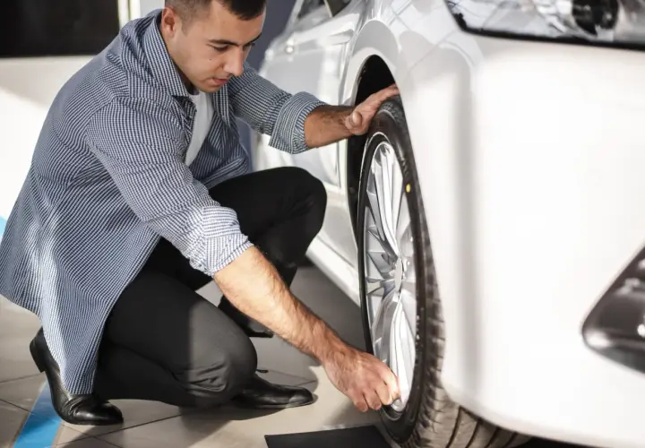 Hombre revisando la rueda de un coche blanco, asegurándose de que el neumático tenga el código velocidad correcto para un viaje seguro.